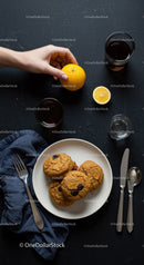 Hand Reaching for Fresh Orange Near Plate of Cookies