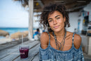 Young Woman Relaxing at Beachside Cafe with Berry Juice Under Sun