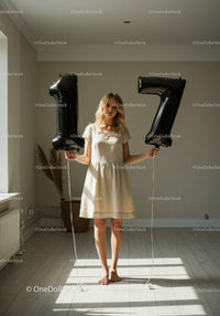 Young woman holding black number balloons in bright room