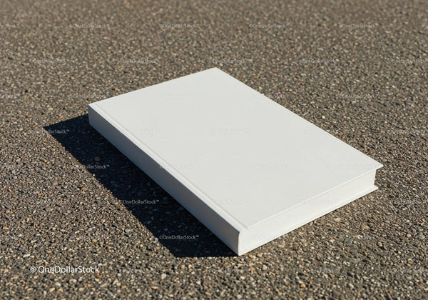 Closed white book resting on rough asphalt surface JPG Mockup Image