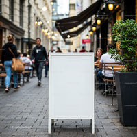 Empty White Sidewalk Sign in Vibrant Urban Cafe Street