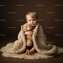 Toddler wrapped in knitted blanket hugging teddy bear