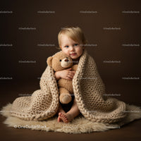 Toddler wrapped in knitted blanket hugging teddy bear