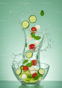 Fresh vegetable ingredients splashing from glass bowl