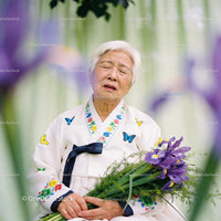 Elderly woman in traditional hanbok holding purple irises