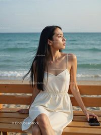 Elegant Woman in White Dress Sitting by Relaxing Seaside Landscape