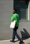Young Man in Green Sweater Walking on City Street with Tote Bag