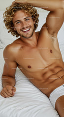 Smiling shirtless man with curly hair relaxing on bed