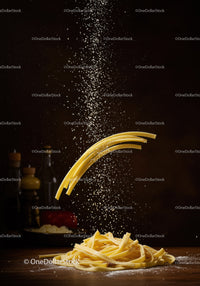 Uncooked pasta and flour falling on wooden surface