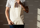 Man Holding Blank Beige Canvas Tote Bag Against Wall