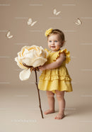 Smiling toddler in yellow dress holding giant flower