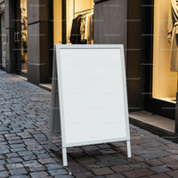 Blank white sandwich board on cobblestone street near store
