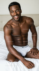 Smiling muscular man sitting on bed in white underwear