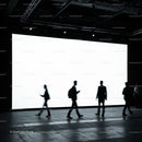 Silhouettes of people walking in front of bright screen
