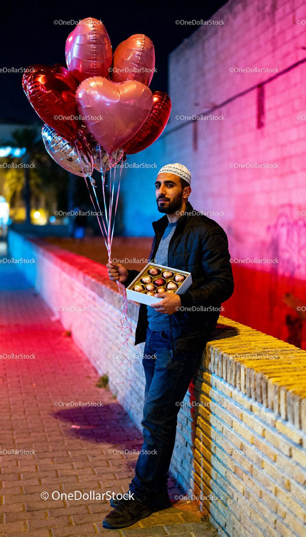 Man Holding Heart Balloons and Chocolates Outdoors at Night