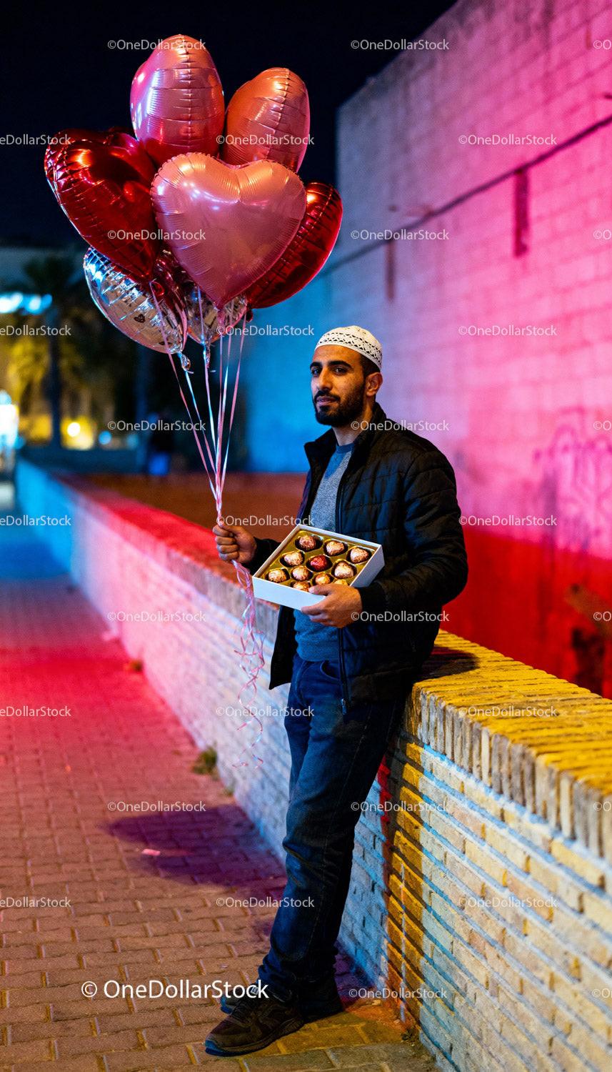 Man Holding Heart Balloons and Chocolates Outdoors at Night