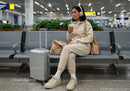 Young Woman Sitting with Suitcase and Coffee in Airport Terminal
