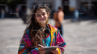 Smiling Young Woman with Colorful Jacket and Laptop in Outdoor City Scene