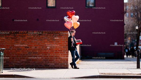 Man waiting with heart balloons and chocolates outdoors