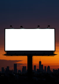 Blank illuminated billboard over city skyline at sunset