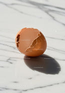Broken brown eggshell casting shadow on marble surface