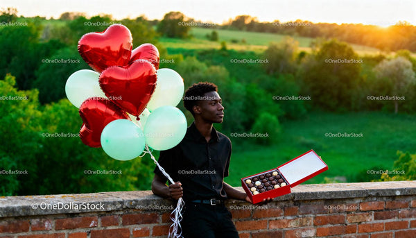 Man holding heart balloons and chocolates outdoors