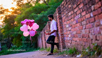 Man holding heart-shaped balloons and chocolates outdoors