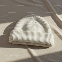 Cozy white knitted beanie hat on soft fabric surface