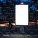 Blank illuminated billboard by city street at dusk