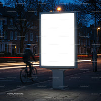 Blank illuminated billboard by city street at dusk