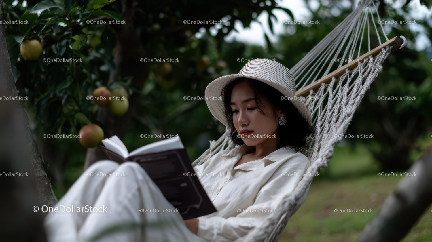 Relaxing Woman Sitting in Hammock Reading in Apple Orchard