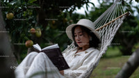 Relaxing Woman Sitting in Hammock Reading in Apple Orchard