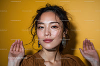 Elegant Young Woman with Curly Hair and Earrings on Yellow Background