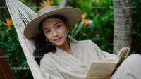 Young Woman Relaxing in Tropical Garden Hammock Reading Book