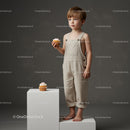 Thoughtful toddler boy in beige overalls with cupcake