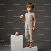 Thoughtful toddler boy in beige overalls with cupcake
