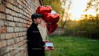Young man holding heart balloons and chocolates outdoors
