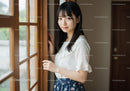 Young Woman Standing By Window In Casual White Blouse And Floral Skirt