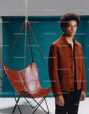 Young man in brown jacket standing near leather chair