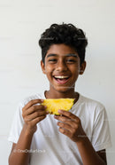 Joyful boy enjoying fresh pineapple slice in bright casual setting