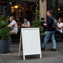 Blank white board at bustling outdoor cafe seating area