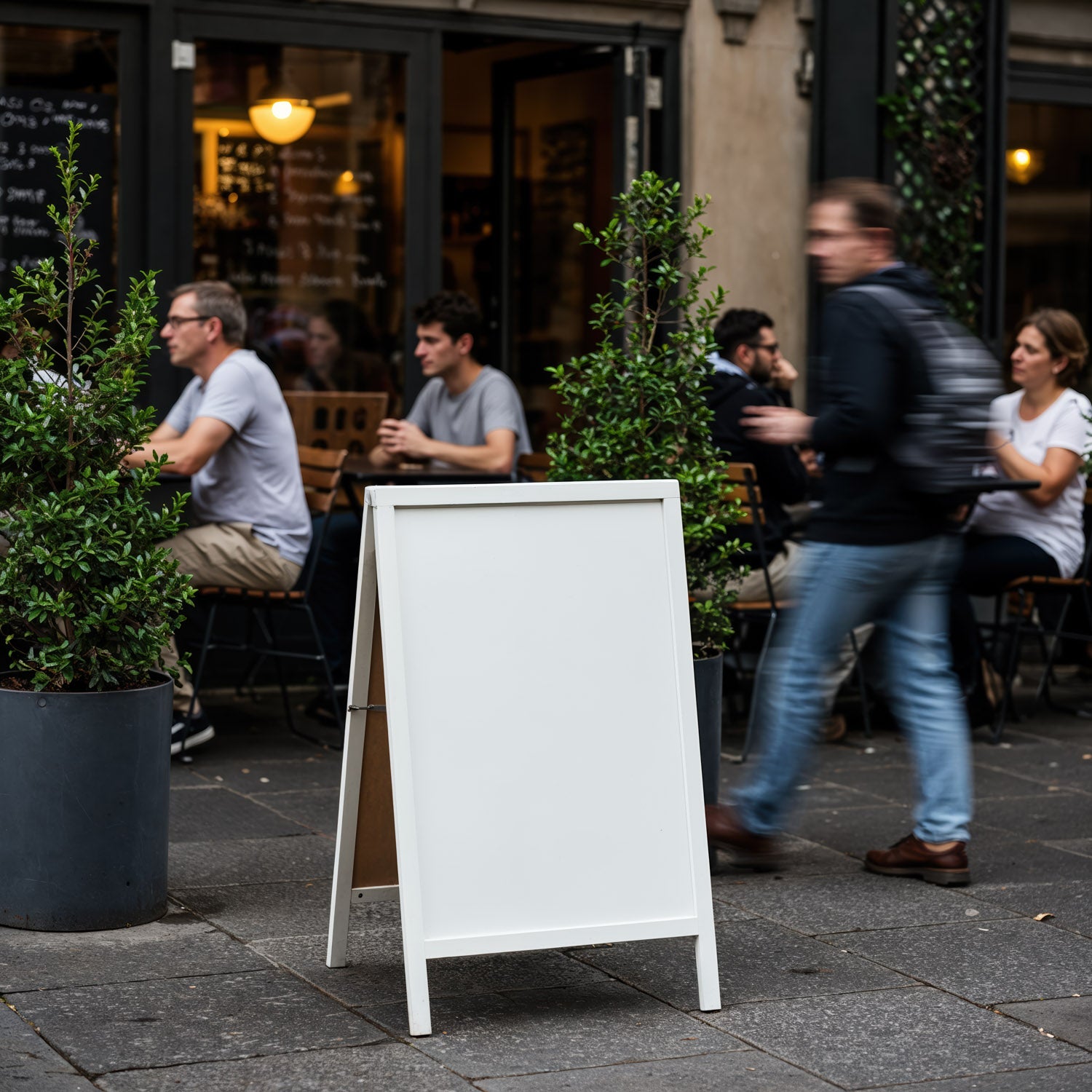 Blank white board at bustling outdoor cafe seating area