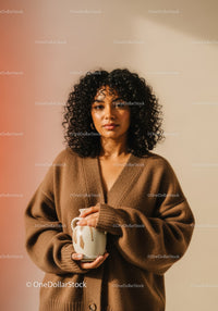 Portrait of a Woman with Curly Hair Holding a Mug in Cozy Sweater