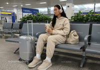 Young Woman Relaxing at Airport with Suitcase and Coffee