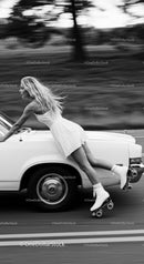 Young woman roller skating alongside classic white car