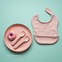 Baby feeding set with bib and toy donut on pastel background