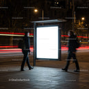 Two men walking past illuminated bus stop ad at night