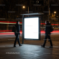 Two men walking past illuminated bus stop ad at night