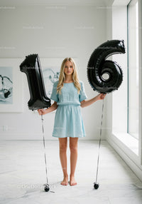 Teenage girl holding black balloons shaped as number sixteen