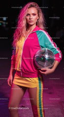 Vibrant Young Woman in Colorful Tracksuit Holding Disco Ball at Night